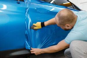 Mechaniker installiert eine schützende Vinylfolie oder -folie an einer Fahrzeugtür.