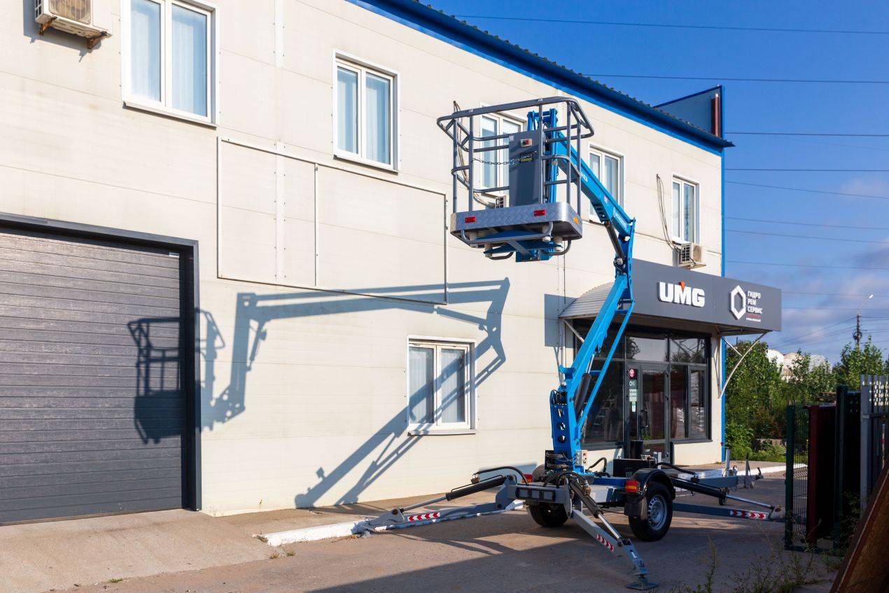 Blauer Minikran hebt Arbeitsbühne an Fassade eines Industriegebäudes