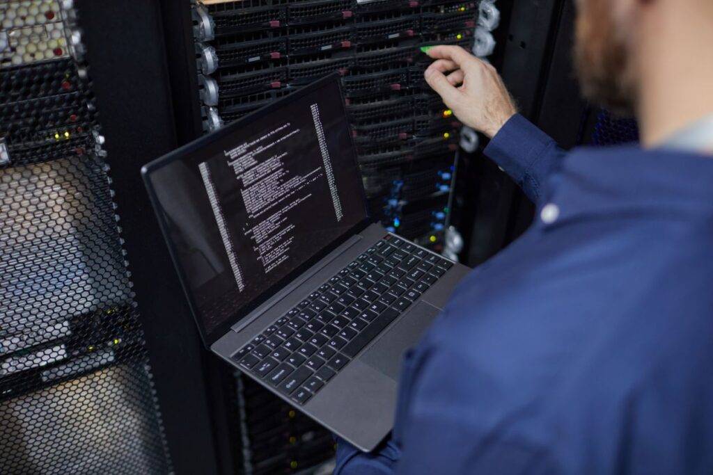 IT-Techniker arbeitet mit Laptop an MTP-Verbindungen im Netzwerkschrank eines Rechenzentrums, Kontrolle der Infrastruktur in Echtzeit