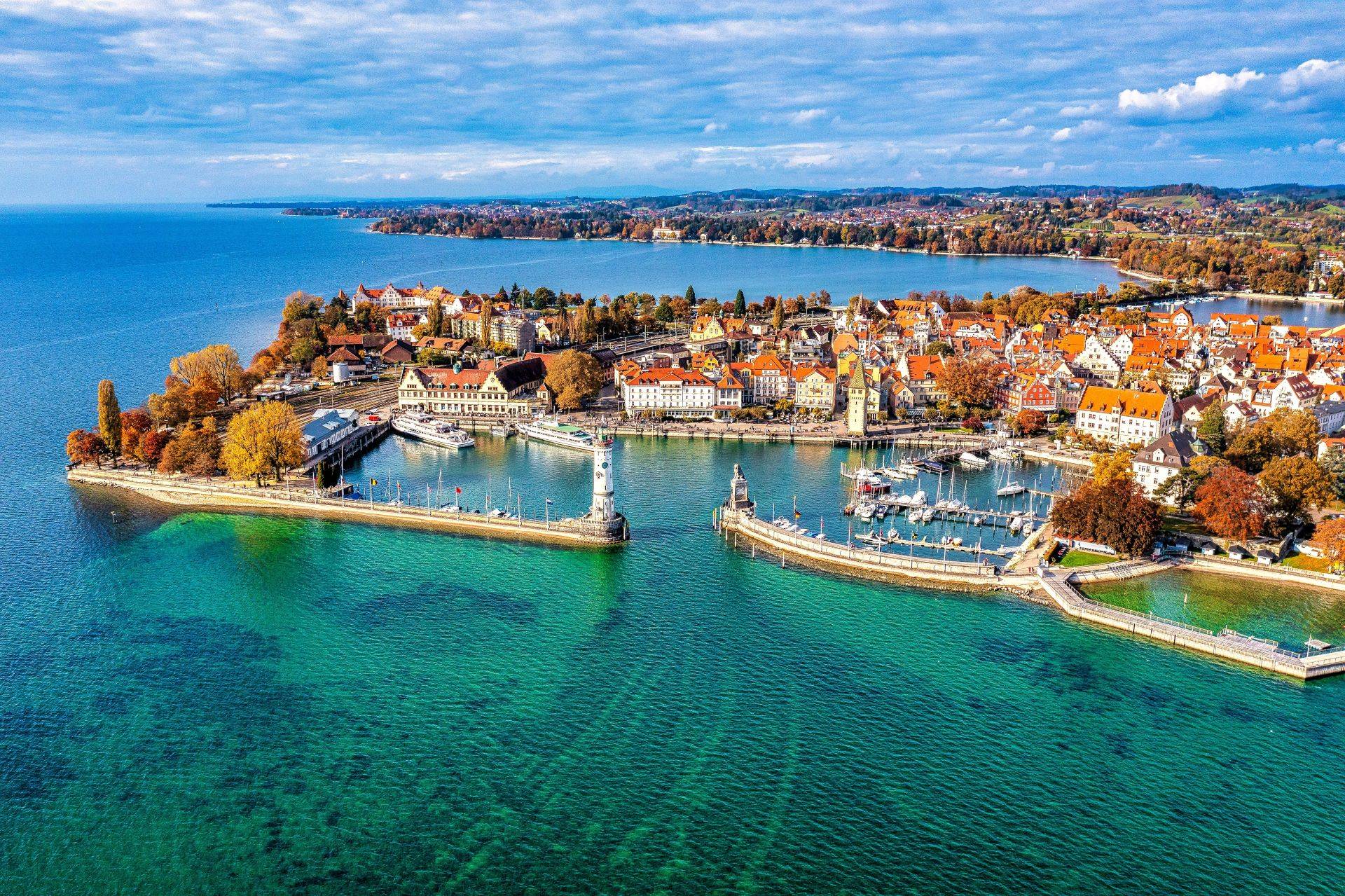 Blick auf den Hafen von Lindau am Bodensee mit Leuchtturm, Altstadt und Alpenpanorama bei klarem Wetter